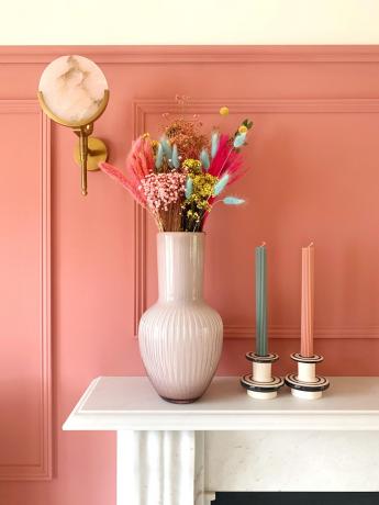 Camino decorato con fiori secchi e candele contro la parete rosa fragola con finiture