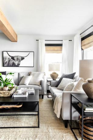 Ein modernes, rustikales Wohnzimmer mit neutralen Beige- und Schwarztönen, grauen Sofas und natürlichen Texturen, darunter geflochtene Körbe und Lampenschirme aus Leinen