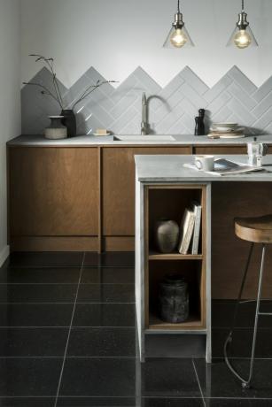 Černé žulové podlahové dlaždice v kuchyni s rybími bílými a šedými obklady, mramorovým kuchyňským ostrůvkem a dřevěnými sedacími barovými židlemi