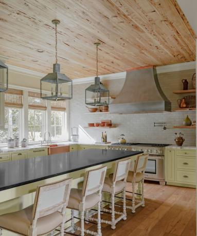 Svetinga, jauki virtuvė su suderintomis medinėmis grindimis ir lubomis bei trijule žibintų pakabučiais, kabančiais virš salos