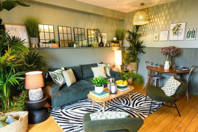 Camera verde salvia con divano in velluto, sedie verde bouclé, tappeto grafico bianco e nero sotto il tavolino con piante in vaso intorno