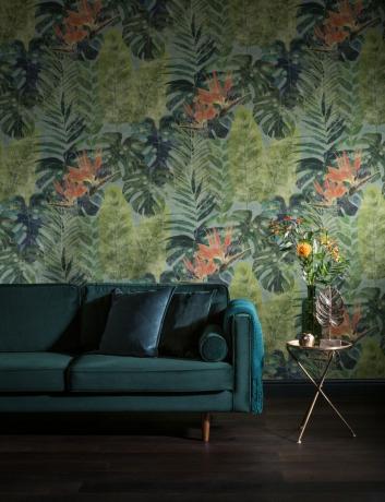 wallpaper berdaun tropis di ruang tamu dengan sofa beludru biru oranye dan hijau