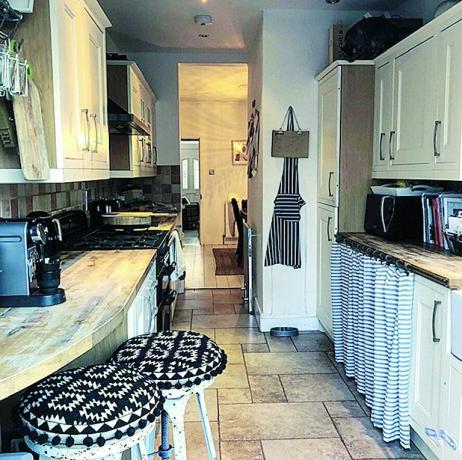 Vorheriges Bild der Küche mit cremefarbenen Schränken, Steinboden und Boho-Barhockern