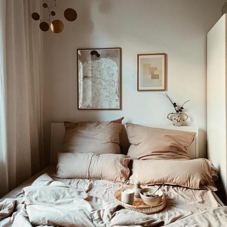 Rahat çarşaflar ve yatak tepsisinde kahvaltı içeren rahat, nötr yatak odası düzeni