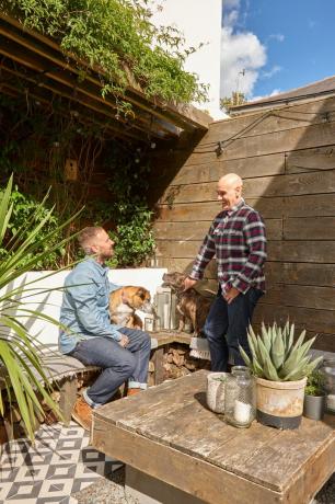 Σπίτι του Jason Traves: Οι ιδιοκτήτες σπιτιού κάθονται στην αυλή τους με ανακυκλωμένο πάγκο παλέτας και τραπεζάκι σαλονιού, δάπεδο με πλακάκια