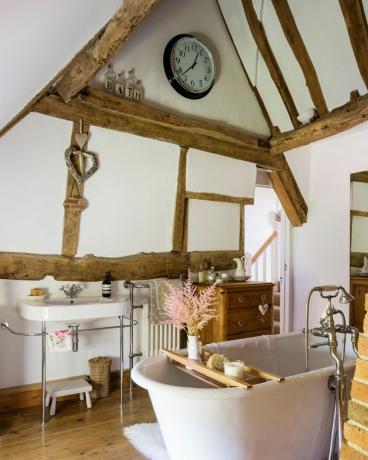 חדר אמבטיה מסורתי עם כלי סניטריה קרמיים לבנים וקורות חשופות