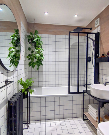 白いタイルとクリティカルスタイルのシャワースクリーン、マットな黒のラジエーター、丸い鏡を備えたバスルーム