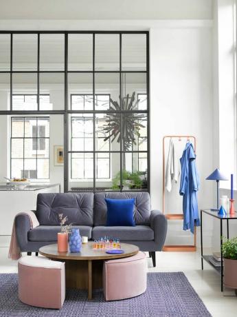 オープンプランのスペース、灰色のソファ、スツール付きのコーヒーテーブル、青い敷物、白い床、黒いコンソール付きの白いリビングルーム