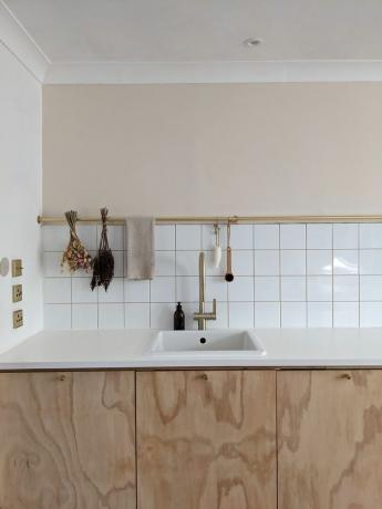Pia de cozinha branca com utensílios pendurados e azulejos brancos embaixo da metade da parede pintada