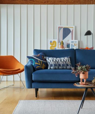 синий диван и оранжевое кресло на фоне белой обшитой панелями стены с журнальным столиком