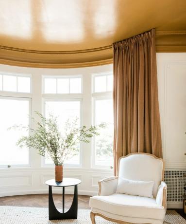 Hvite vegger og gult kontrasttak på soverommet med gule gardiner som rammer inn karnappvinduer