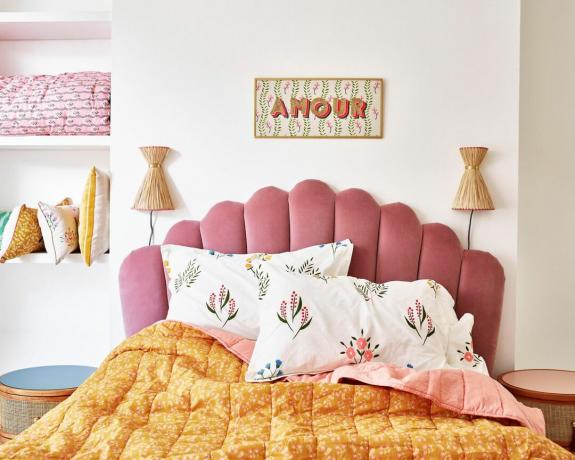 Una idea de iluminación de pared de dormitorio de Oliver Bonas con un par de luces de trabajo de pared de rafia, cabecero festoneado y ropa de cama floral
