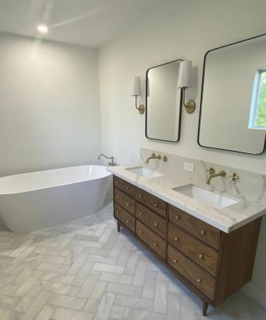 हेरिंगबोन फर्श सजावट, ड्रेसर वैनिटी यूनिट और सफेद बाथटब के साथ एक आधुनिक बाथरूम