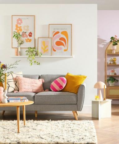 Ein kleines Wohnzimmer mit einer grauen Couch, einem Bücherregal und Wandkunst