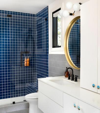 bagno blu con doccia piastrellata blu, panca doccia, pareti bianche, lavabo bianco, piastrelle grigie, specchio dorato