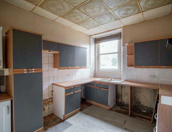 Posnetek 'pred', ki prikazuje kuhinjo s sivimi in lesenimi enotami ter stropom s ploščicami
