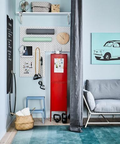 Nastavení domácí posilovny v modrém obývacím pokoji s tmavě šedým rozdělovačem záclon, červenou retro skříňkou, bílým kolíčkem