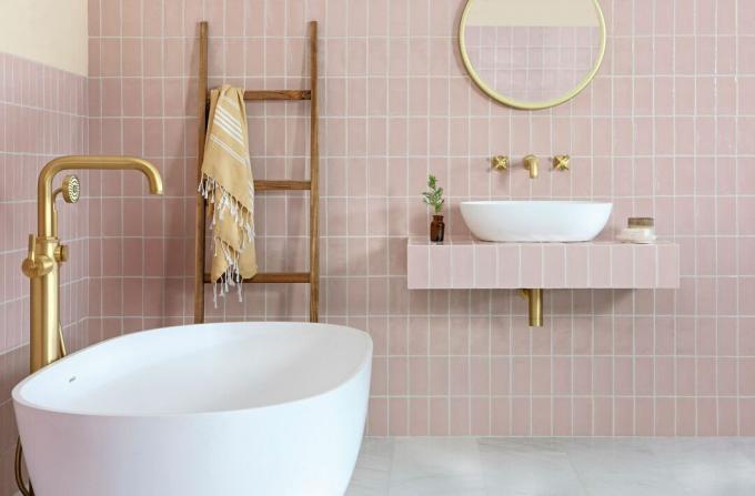 Ubin merah muda dengan nat putih di kamar mandi lengkap dengan lantai abu-abu batu tulis, bak putih dan aksen emas