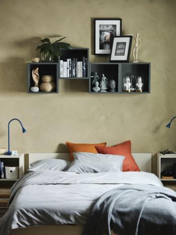 miegamasis su smėlio spalvos sienomis, lentynomis virš lovos, pilka ir oranžinė patalynė