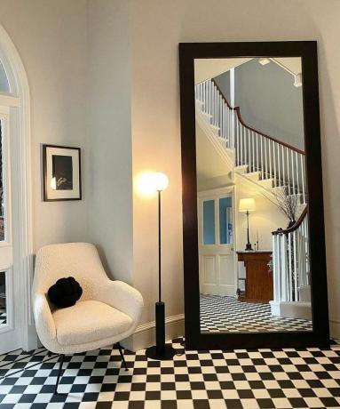 Espelho longo de corredor preto com cadeira boucle Made.com e piso xadrez monocromático