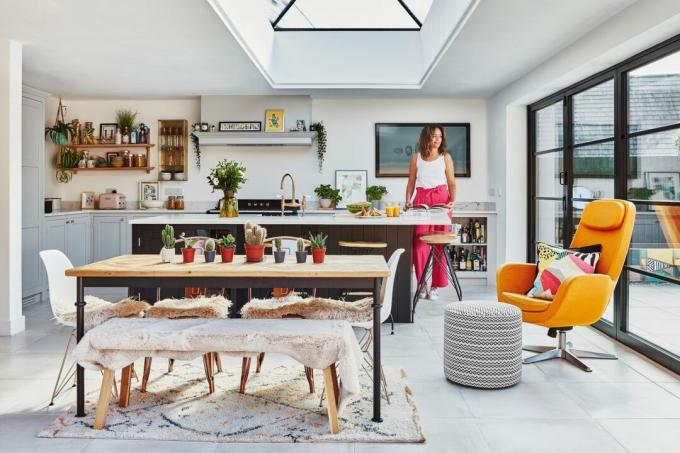 Grote open keuken-eetkamer-uitbreiding met grijze grootformaat vloertegels, zwarte en houten eettafel, gele fauteuil en donkerblauw-zwarte Shaker-keuken