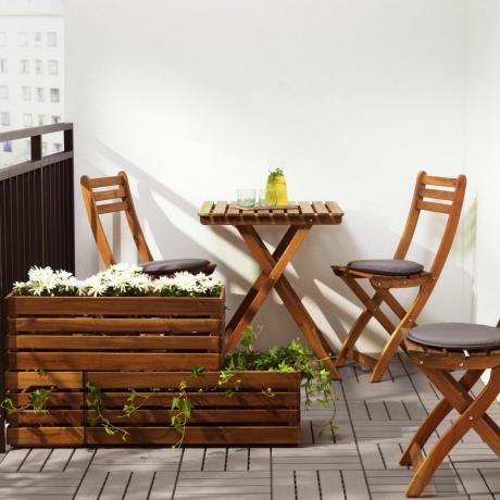 Jardiniere din lemn pentru ferestre cu flori albe și iederă pe balcon mic, cu set de bistro de grădină din lemn