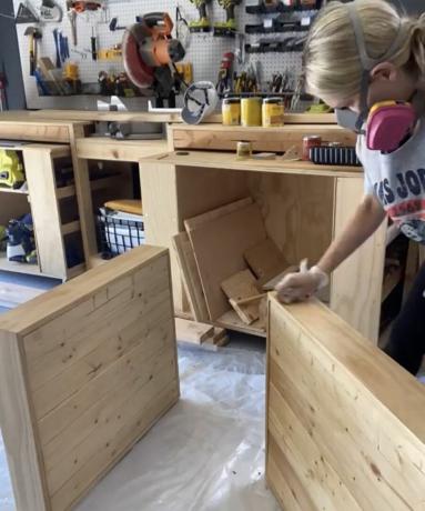 गैरेज में लकड़ी के आउटडोर सोफा फ्रेम का DIY निर्माण करते समय ब्रुक वेट ने सुरक्षात्मक धूल मास्क पहना हुआ था