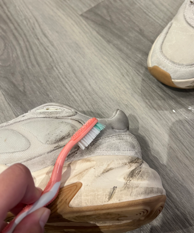 En rosa tannbørste som skrubber en nøytral joggesko