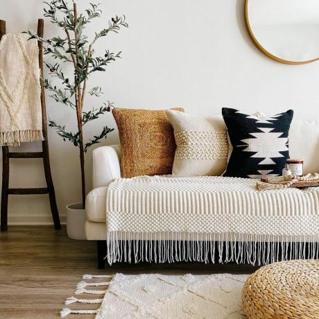 Splendido soggiorno boho con cuscini pesanti e tattili sul divano, con tappeto strutturato e pouf sul pavimento naturale