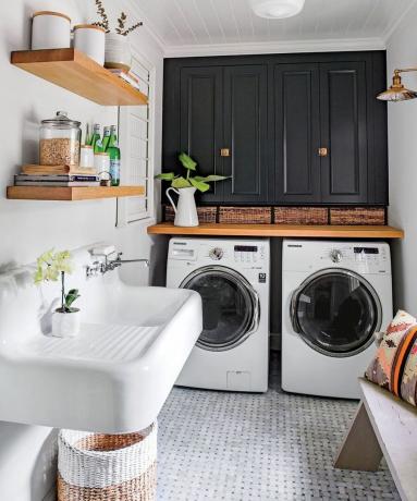 Zona lavanderia mudroom piastrellata in marmo con lavello, scaffalature in legno, doppia lavatrice e cestini