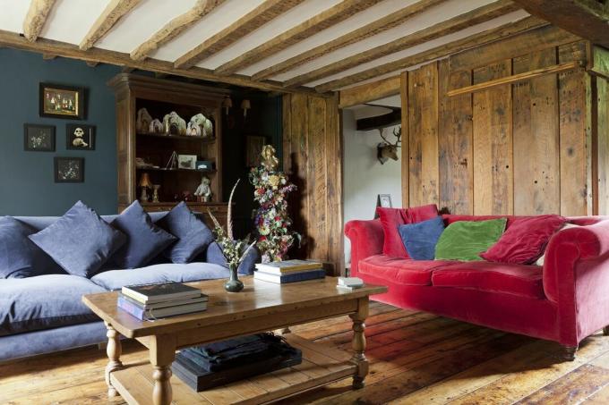 cameră de zi cu pereți din lemn, cu grinzi și canapele din catifea roșie și albastră și podele din lemn