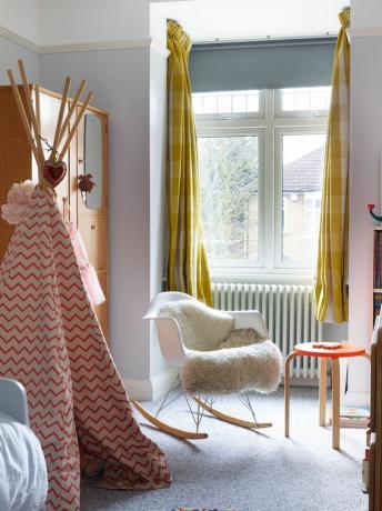 dormitorio para niños con tipi, mecedora, alfombra gris y taburete naranja