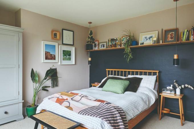 Lea-Wilson namas: pagrindinis miegamasis su rožinėmis sienomis, lentyna nuo sienos iki sienos su lova su tamsiai mėlyna spalva, apačioje, spalvingas abstraktus metimas ir rotango stalas lovos gale