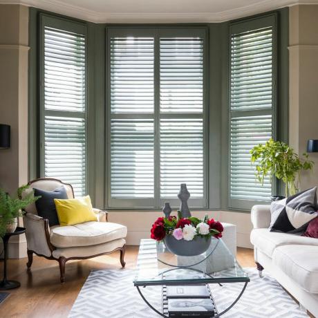 Erkerfenster mit grünen Vollholzfensterläden und cremefarbener Stoffcouch, Sessel und Teppich
