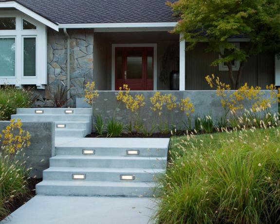 O curte modernă din față cu trepte din beton și iarbă