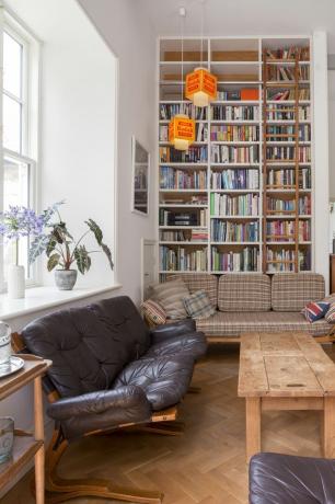 صوفا سوداء وأريكة مربعة في غرفة المعيشة أمام رف الكتب مع الكثير من الكتب