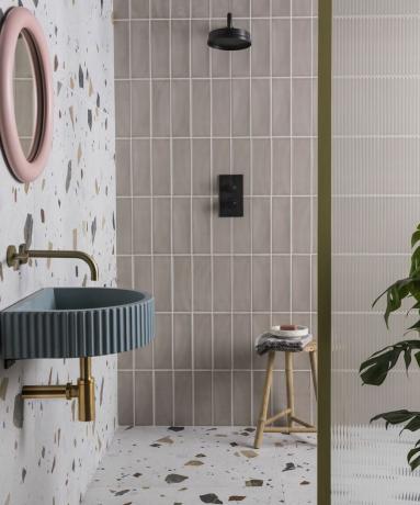 Smėlio spalvos vonios kambario idėja su mokos blizgiomis plytelėmis, rožiniu veidrodžiu ir mėlyna kriaukle