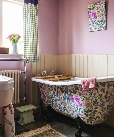 Fürdőszoba rózsaszín falakkal, virágos falfestményekkel és virágmintával díszített káddal