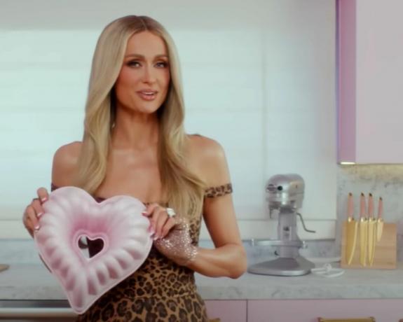 Paris Hilton segurando um molde de assadeira em forma de coração com um bloco de faca rosa em forma de coração no fundo
