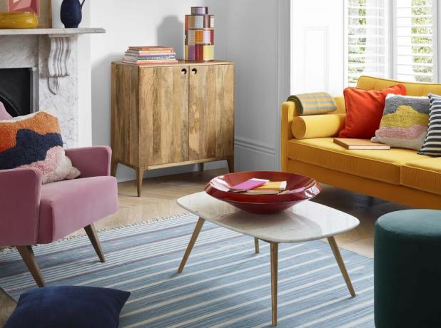 黄色いソファ、ピンクのアームチェア、木製のコーヒーテーブルを備えたミッドセンチュリースタイルのリビングルーム
