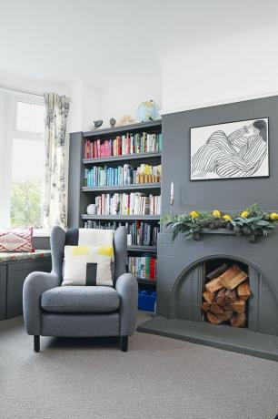 Šedý obývací pokoj s otevřenými policemi plnými knih, šedým křeslem a krbem plným polen, s orámovanou monochromatickou kresbou nahoře