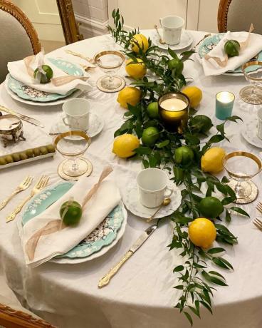 Corda de limões e limas na mesa redonda vestida com toalha de mesa de cetim e pratos azuis ditsy