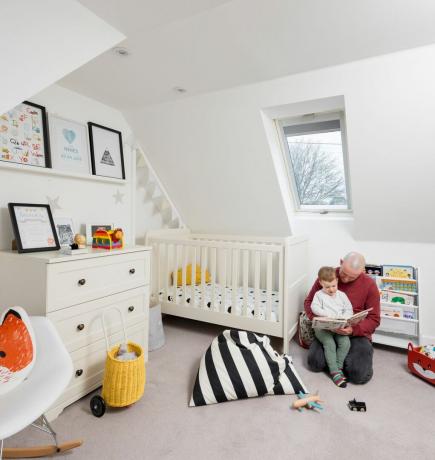Una cameretta per bambini con una combinazione di colori bianca che include un costo, cassettiera e scaffali per libri illustrati per bambini