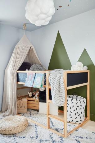Детска стая с бели стени и ефект на зелена планинска боя, дървено двуетажно легло с балдахин, бяло и черно бохо килим и висяща лампа в облак