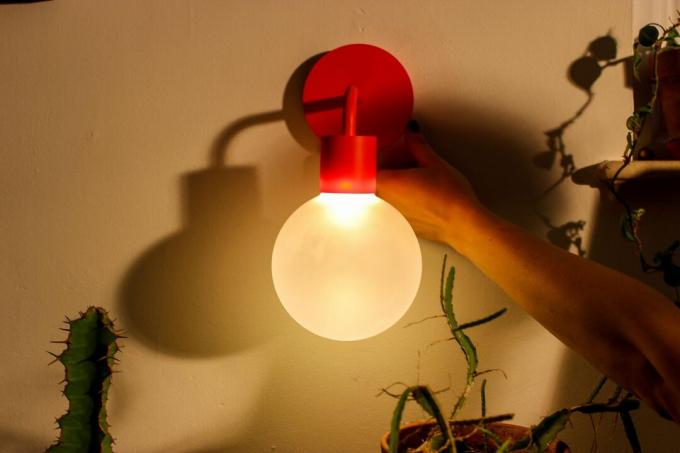 Червена електрическа лампа с ръка и растение близо до нея