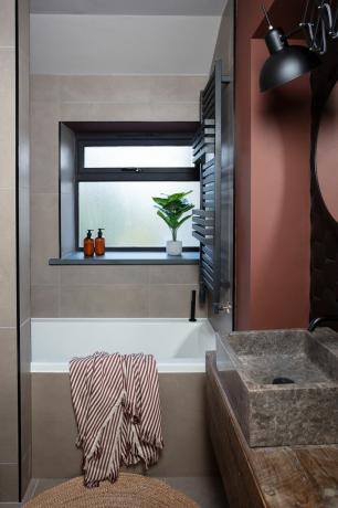 Baño pequeño con azulejos marrones, paredes pintadas de color burdeos y lavabo de piedra