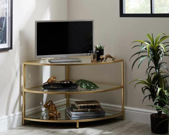 Porta tv ad angolo Claudia effetto oro decorato con accessori accanto alla pianta