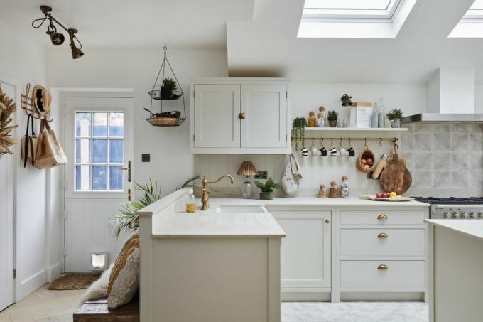 Бяла кухня с модули в стил шейкър, бял работен плот, месингови аксесоари и панелен панел