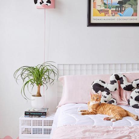 Легло със светло розово спално бельо и растение наблизо