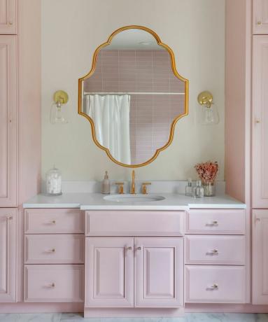 Esquema de banheiro rosa claro com espelho de parede dourado em forma de declaração